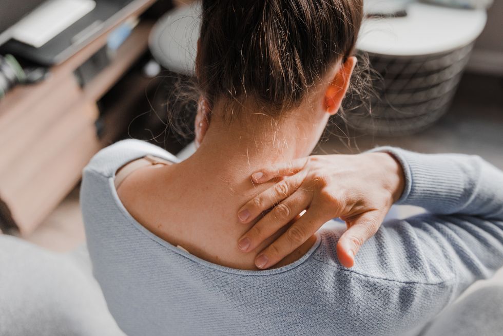 Woman massaging sore neck with hand, wearing a blue sweater, seeking pain relief at home.