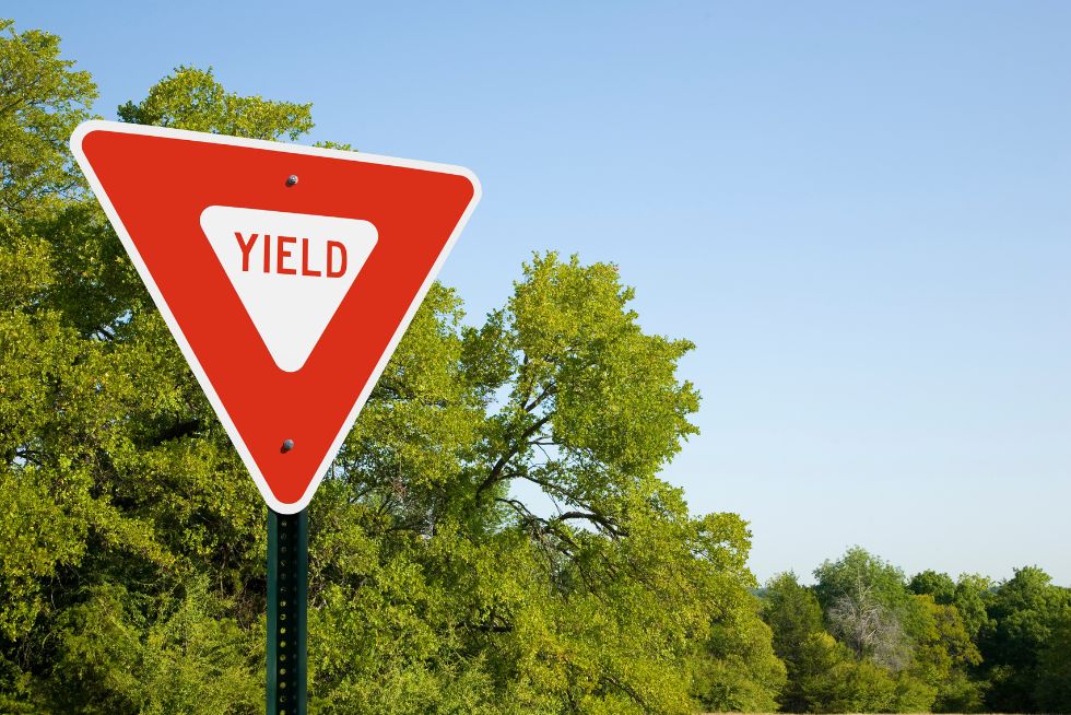 Red yield sign on a sunny day with green trees in the background.