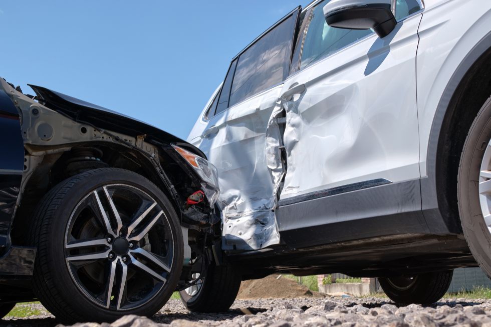 Two cars in a collision, showing significant damage to the front and side under a clear blue sky.